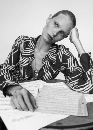 Monochrome portrait of a model in a patterned shirt leaning on a table with musical sheets for 5ELEVEN Magazine