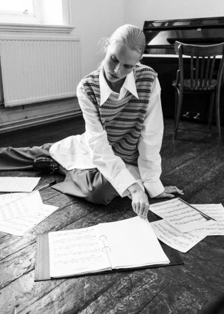 Model Sasha Dom seated on a wooden floor turning sheet music in a room with a piano, photographed by Edwin S Freyer for 5ELEVEN Magazine.