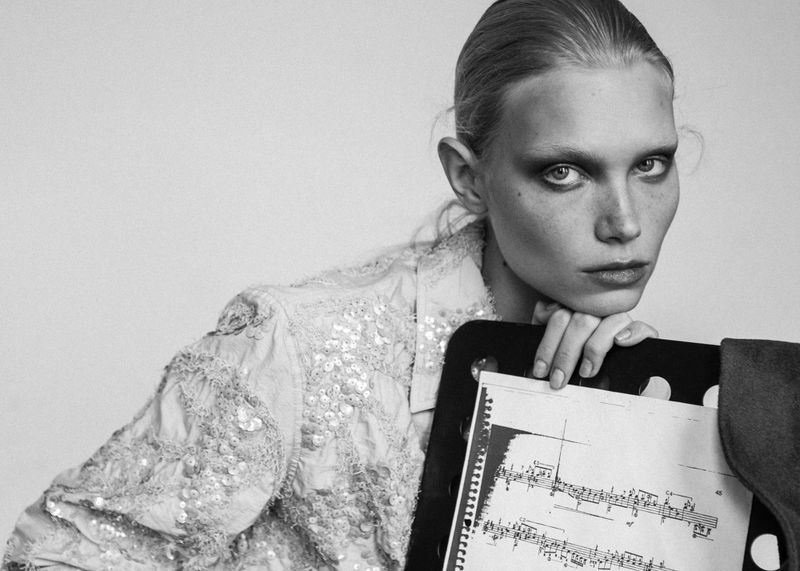 Model resting chin on hands behind a sheet of sheet music in a black and white editorial portrait for 5ELEVEN Magazine