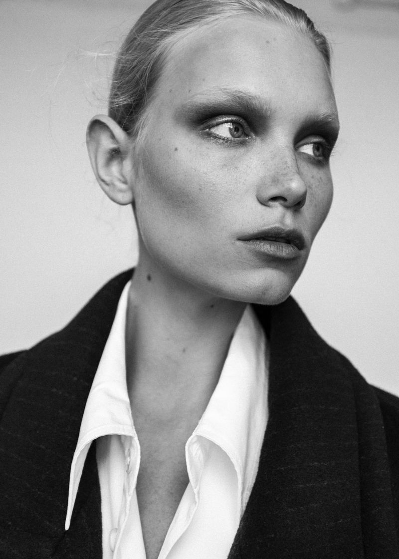 Close-up portrait of a model wearing a white collared shirt and dark outerwear against a plain background