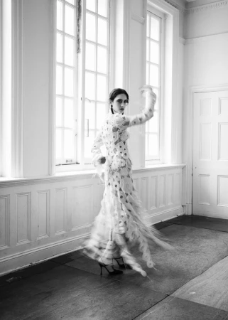 Model in a patterned white dress posing in motion against tall windows for 5ELEVEN Magazine