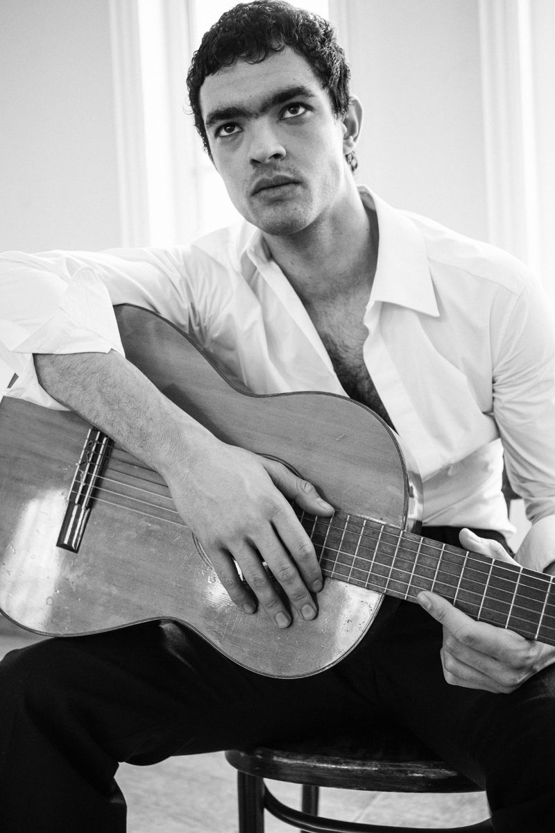 Monochrome portrait of a man in a white shirt holding an acoustic guitar for 5ELEVEN Magazine
