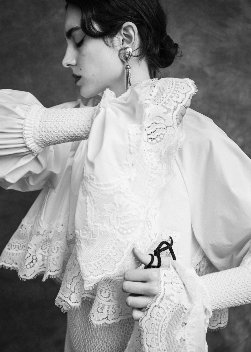 Model in intricate white lace blouse and tassel earrings posing for 5ELEVEN Magazine