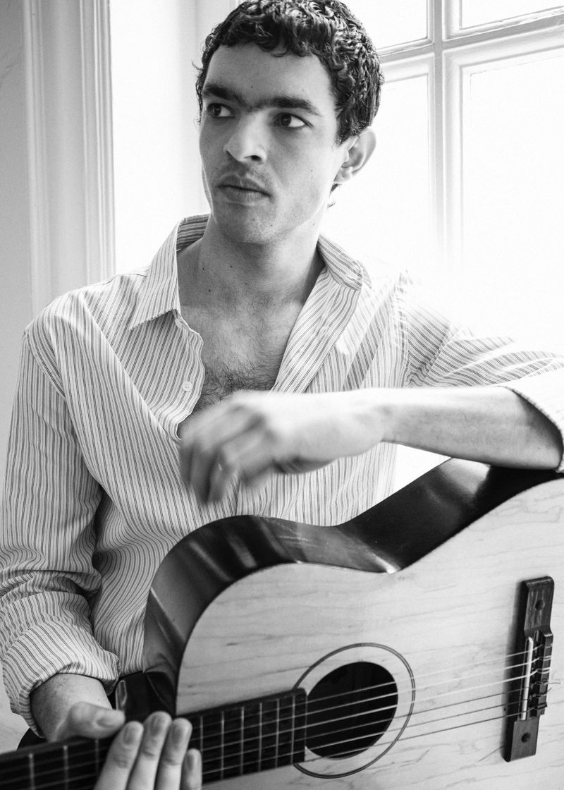 Monochrome portrait of a man in a striped shirt holding an acoustic guitar indoors