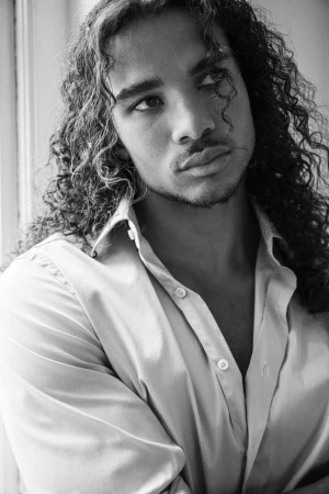Close-up portrait of a man with long curly hair wearing an open-collared button-down shirt.