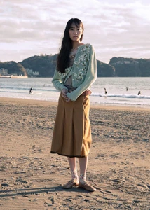 Model wearing a pastel green cardigan and brown skirt standing on a sandy beach for 5ELEVEN Magazine Tasogare project