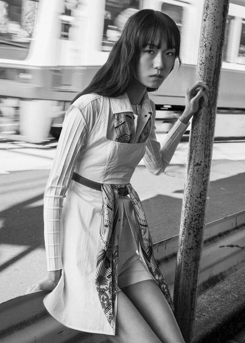 Model in white dress holding pole with motion-blurred train behind in black and white