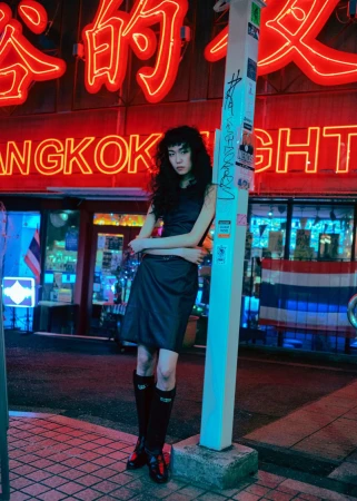 Model Suzune Oda leaning against a post under glowing red neon signs in a street scene for 5ELEVEN Magazine