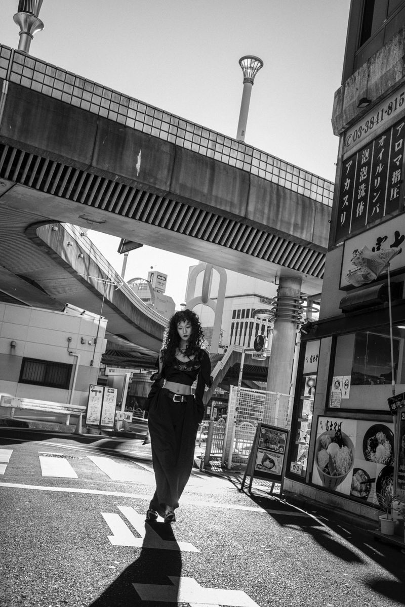 Model Suzune Oda walking on an urban street beneath an elevated highway structure in a black outfit
