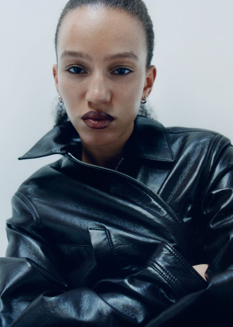 Close-up portrait of a model wearing a glossy black leather jacket against a neutral studio background