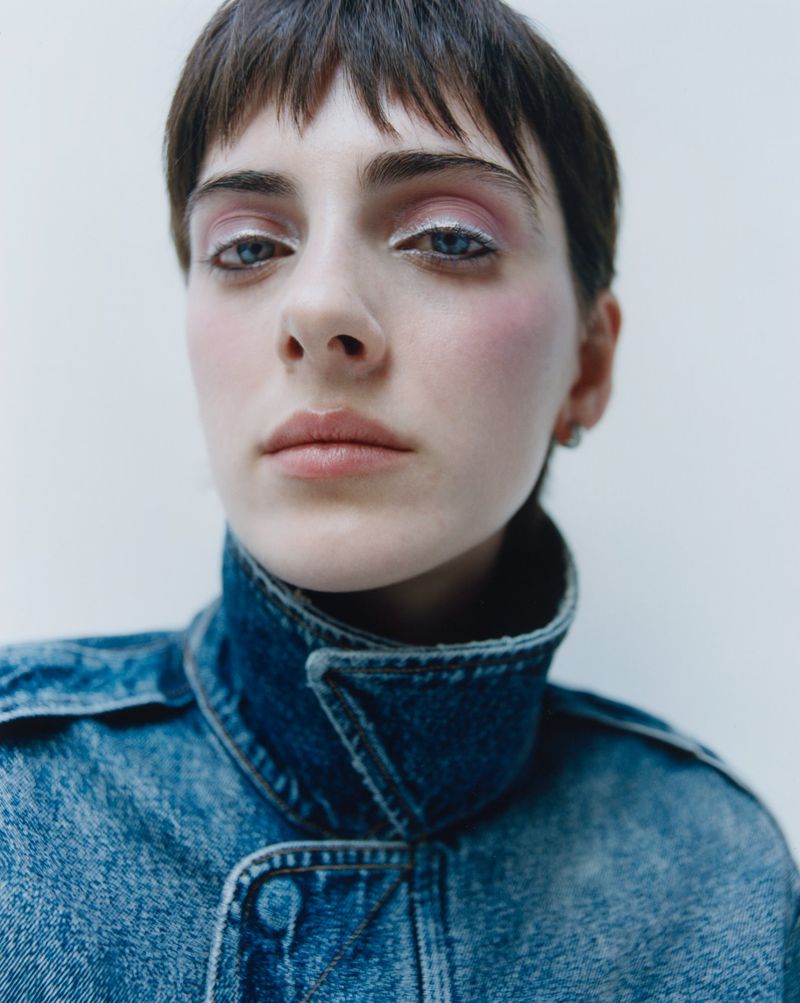 Close-up portrait of a model with short dark hair wearing a blue denim jacket against a neutral backdrop