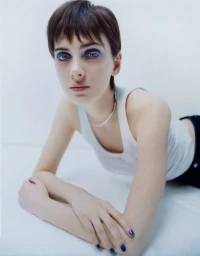 Model with blue eyeshadow and a white tank top leaning forward on a seamless white studio background