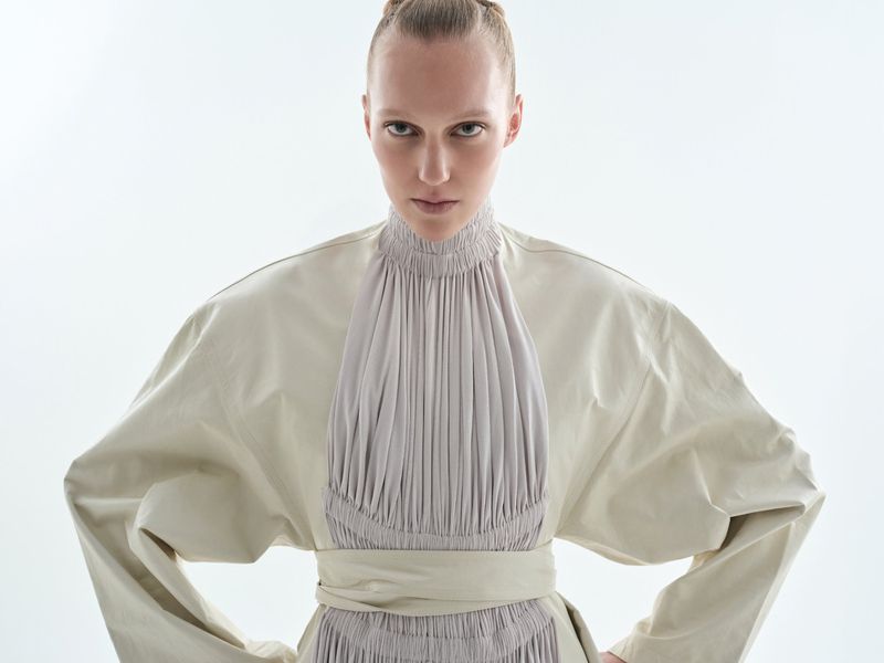 A model wearing a high-collared pleated tunic against a clean white background for Vogue Czechoslovakia.