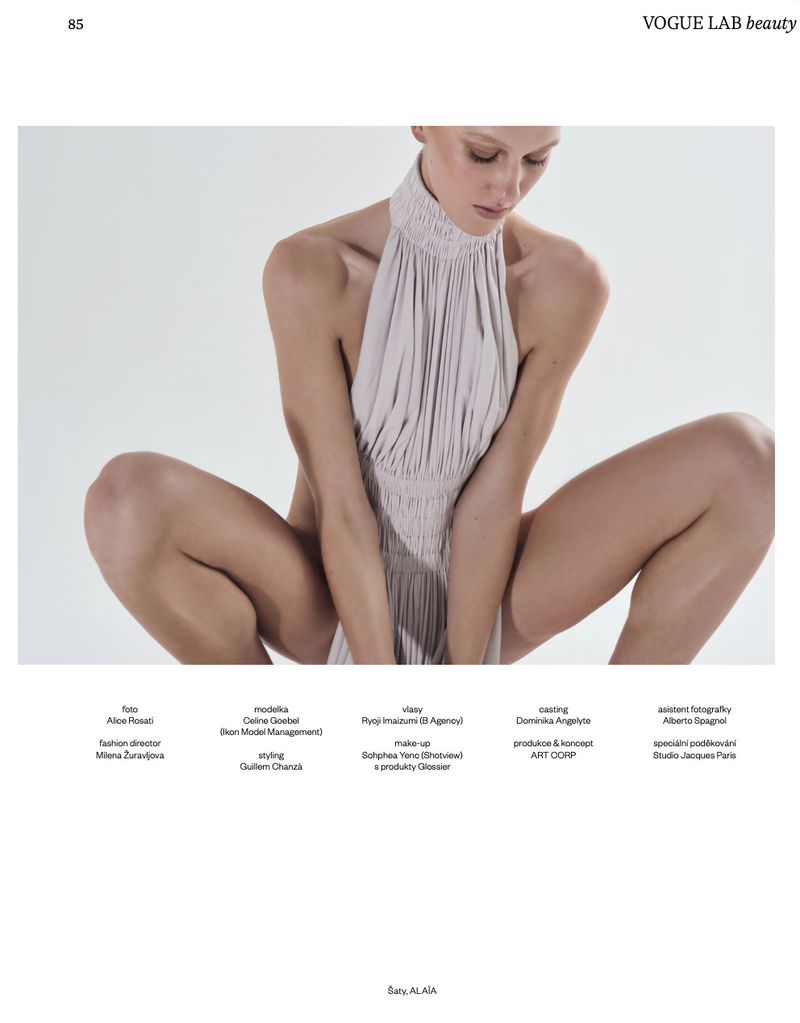 Model wearing a pleated halterneck dress crouching against a plain white studio background for Vogue Czechoslovakia