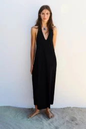 Model in a long black halter dress standing barefoot on sand against a plain white wall for Pull & Bear