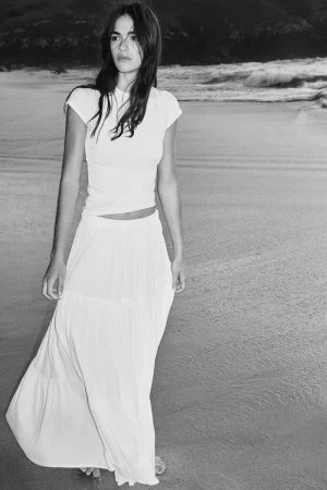 Model in white t-shirt and maxi skirt standing on sandy beach in black and white fashion lookbook photo