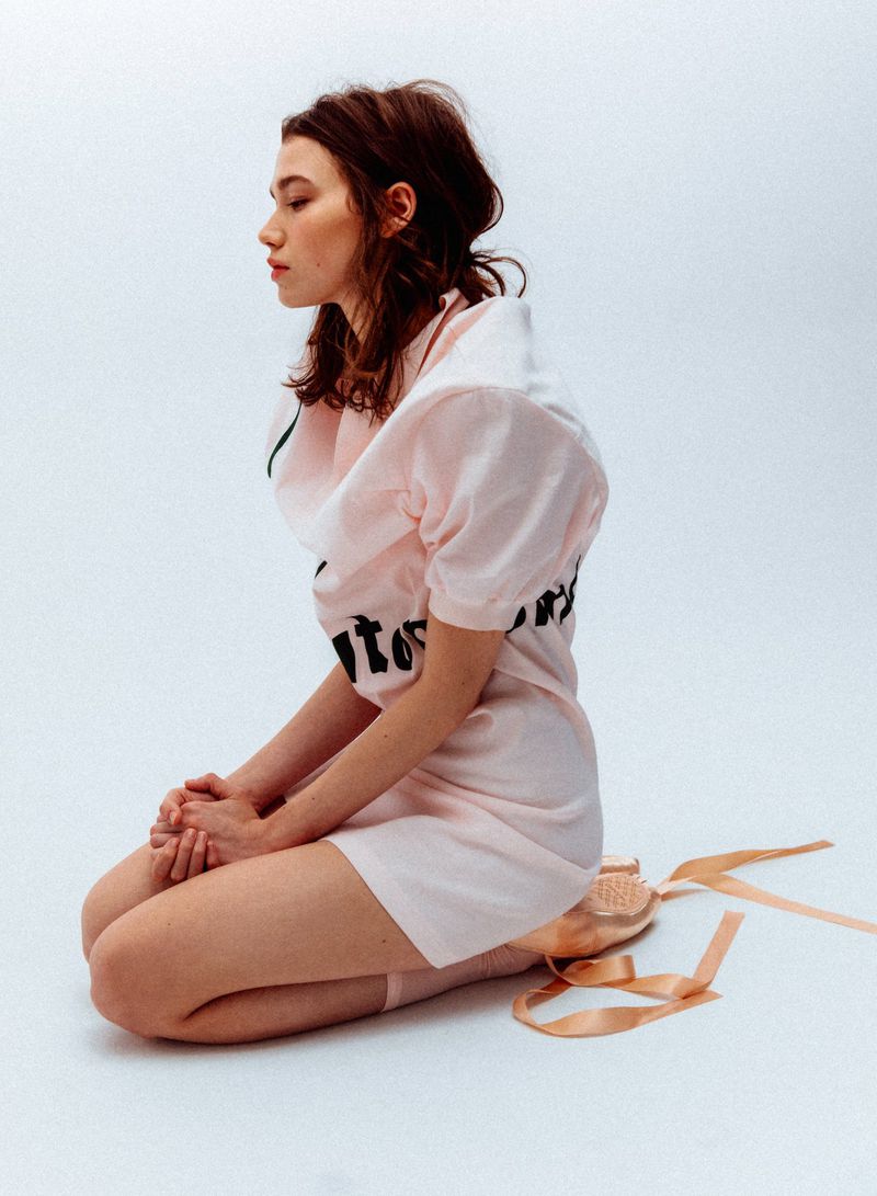 Profile view of a kneeling woman in a pink dress and pointe shoes against a white background for WRPD Magazine.