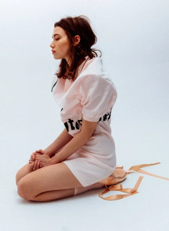 Profile view of a kneeling woman in a pink dress and pointe shoes against a white background for WRPD Magazine.