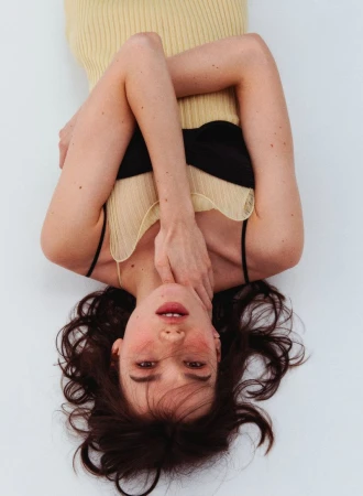 Upside-down portrait of a woman wearing a pale yellow ribbed top and dark bandeau against a white background
