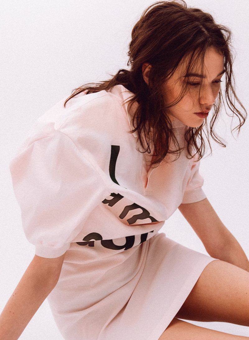 Woman in a pink graphic print t-shirt dress posing against a plain white background for an editorial shoot.