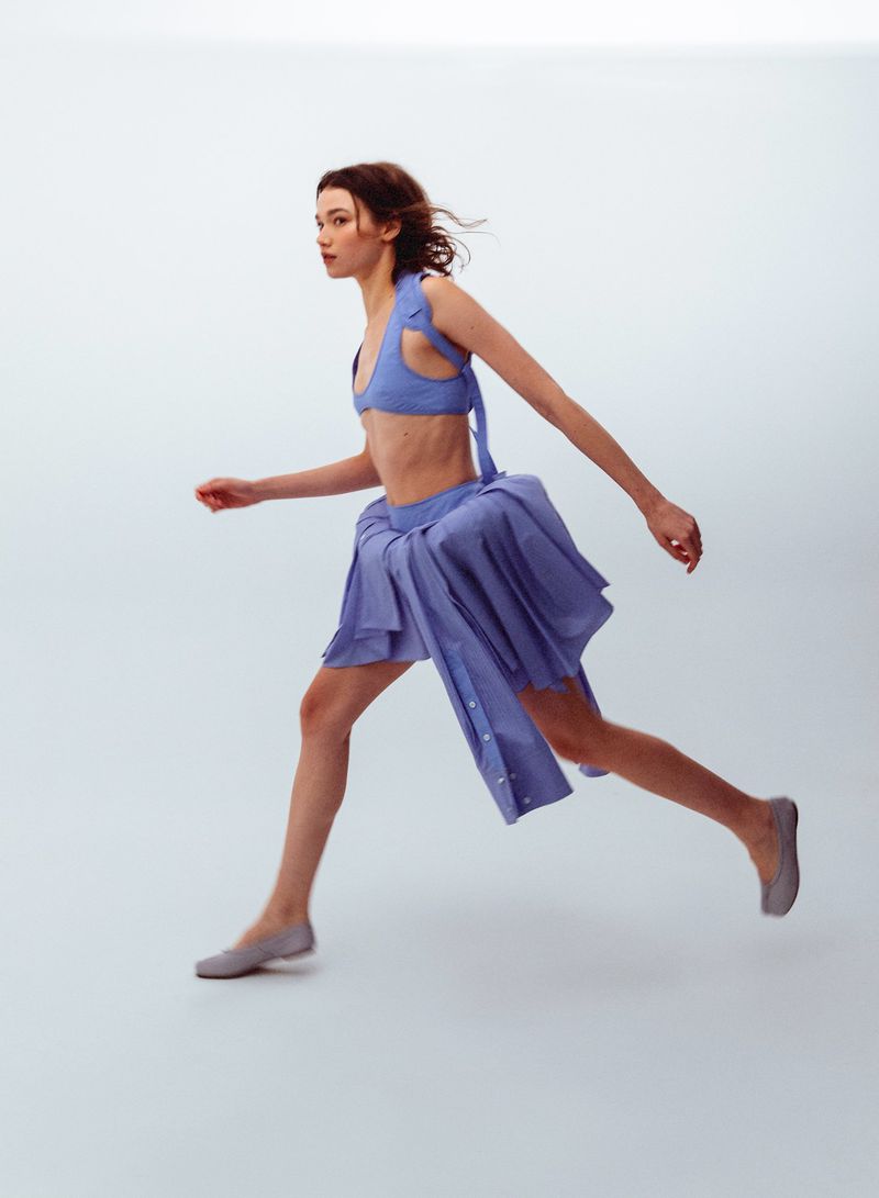 Model in blue two piece outfit and grey flats captured mid stride against a white seamless background for WRPD Magazine.