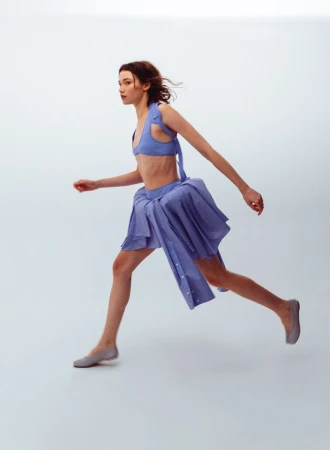 Model in blue two piece outfit and grey flats captured mid stride against a white seamless background for WRPD Magazine.