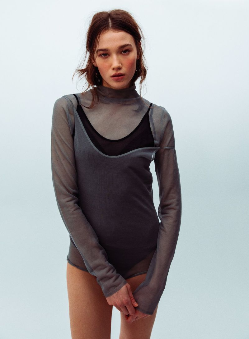 Model wearing a sheer grey turtleneck top over a black slip against a plain light background for WRPD Magazine.
