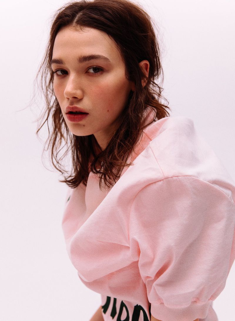 Close-up portrait of a woman wearing a pink top with printed text against a white background
