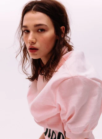 Close-up portrait of a woman wearing a pink top with printed text against a white background