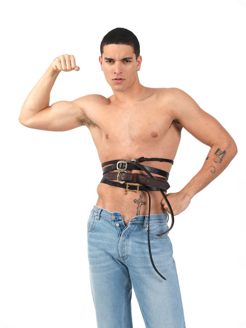 Shirtless male model wearing multiple leather belts around his waist and light blue jeans against a plain white background