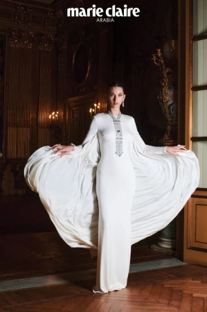 Model Myriem Boukadida in a white gown with dramatic draped cape inside a classical interior for Marie Claire Arabia