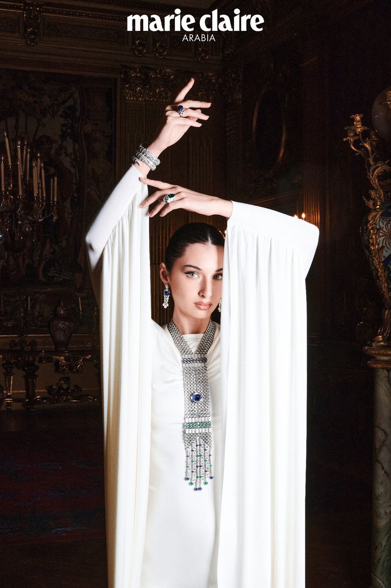 Model Myriem Boukadida wearing a white gown and ornate diamond necklace, posing inside an ornate historic interior.