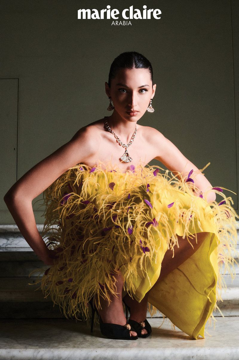 Marie Claire Arabia fashion editorial featuring a woman in yellow feather dress, seated on stairs with dark eye makeup and jewelry.