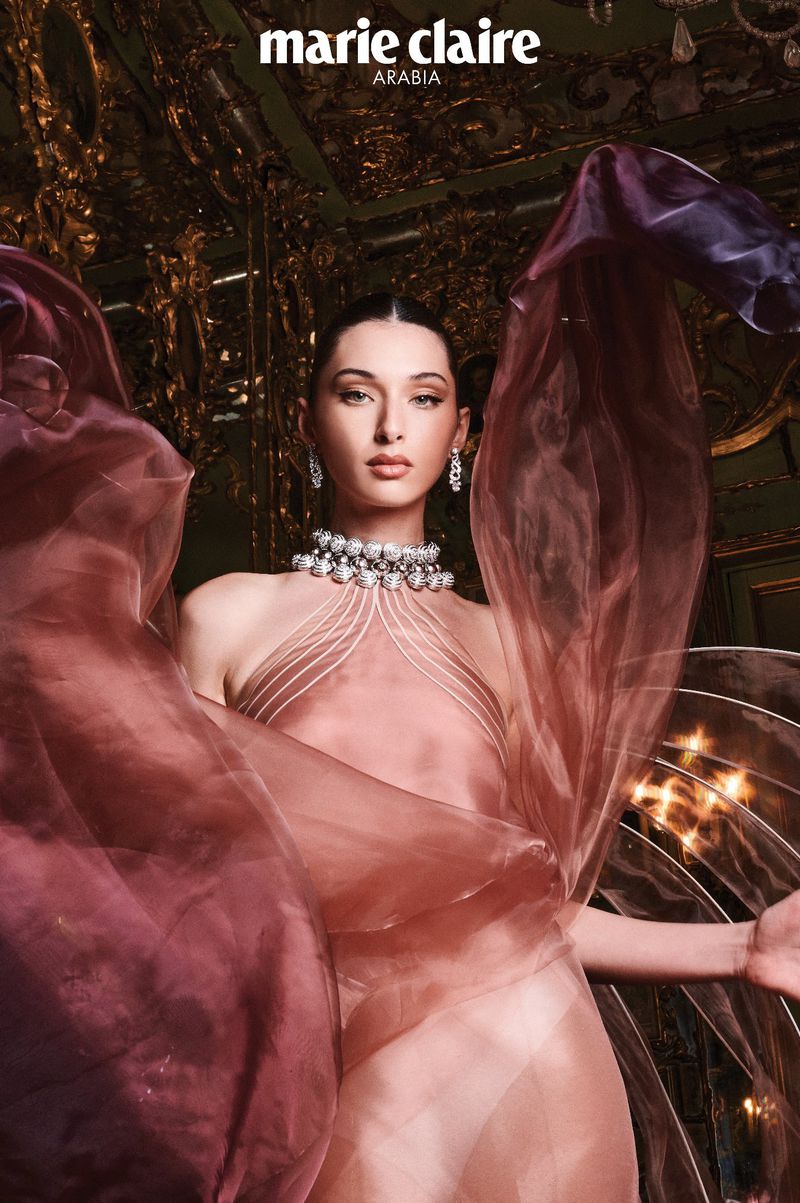 Model Myriem Boukadida in sheer pink halter dress with layered sheer fabric swirling around her in an ornate room