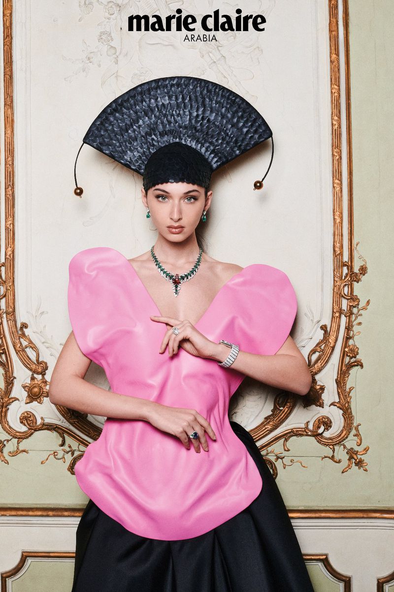 Model Myriem Boukadida wearing a pink structural top, black headpiece, and emerald necklace in an ornate interior for Marie Claire Arabia