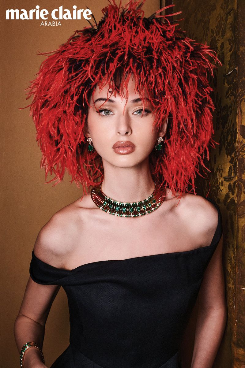 Model Myriem Boukadida wearing a voluminous red feathered hairstyle and black dress with emerald necklace for Marie Claire Arabia