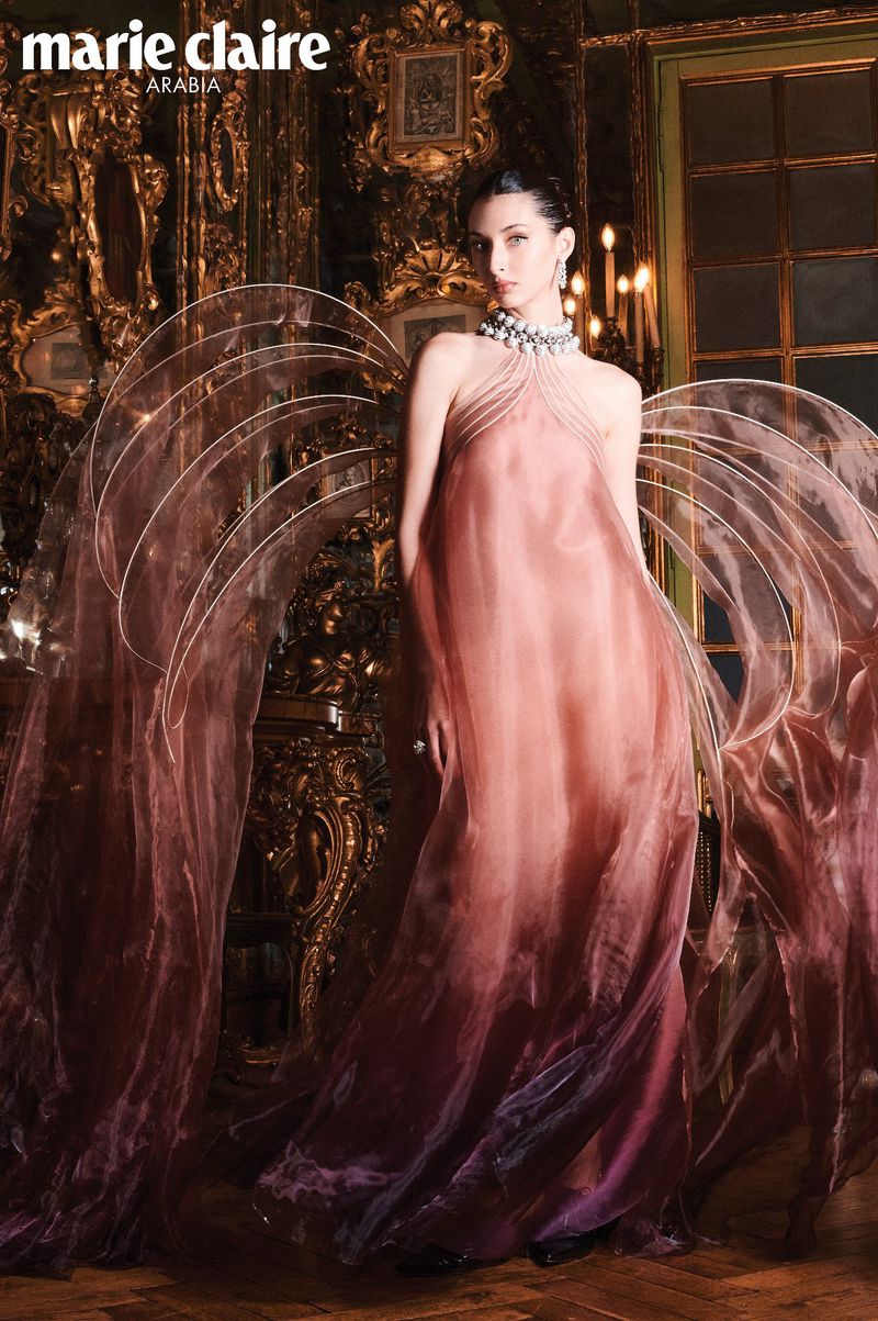 Model Myriem Boukadida in an ombre pink gown with sheer structured wing-like panels in an opulent room