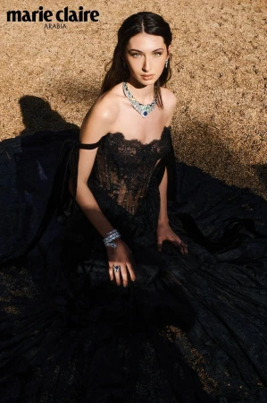 Model Myriem Boukadida in a black lace gown and jewelled necklace seated on sand for Marie Claire Arabia editorial