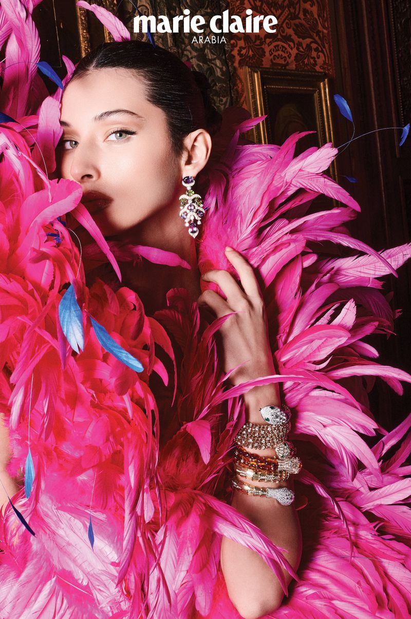 Model Myriem Boukadida surrounded by vibrant pink feathers wearing gemstone earrings and bracelets for Marie Claire Arabia