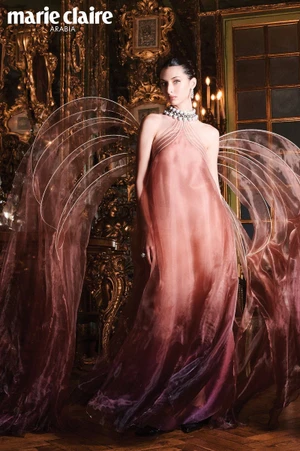 Model Myriem Boukadida in an ombre pink gown with sheer structured wing-like panels in an opulent room