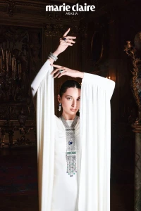 Model Myriem Boukadida wearing a white gown and ornate diamond necklace, posing inside an ornate historic interior.