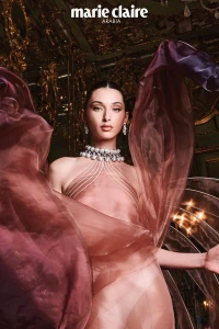 Model Myriem Boukadida in sheer pink halter dress with layered sheer fabric swirling around her in an ornate room