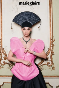 Model Myriem Boukadida wearing a pink structural top, black headpiece, and emerald necklace in an ornate interior for Marie Claire Arabia