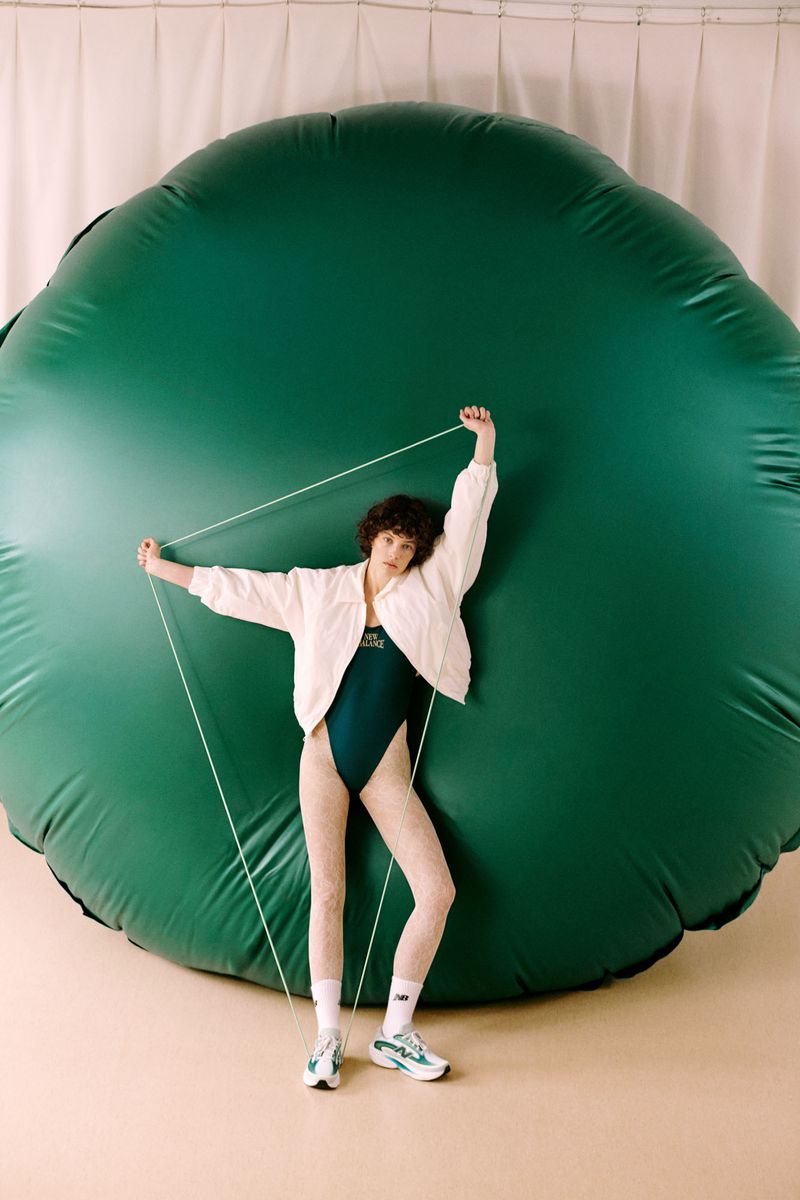 Model in green bodysuit and white jacket posing in front of a giant dark green inflatable sphere for Vogue Polska
