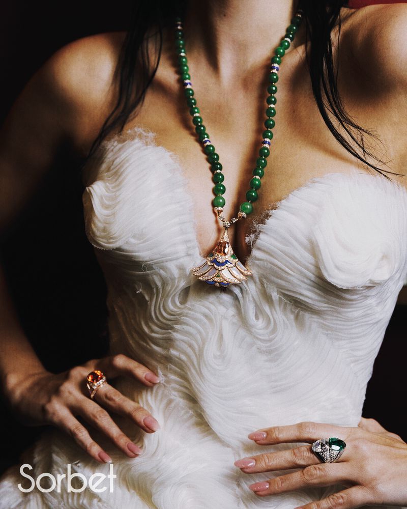 Close-up of a model wearing a textured white dress, a long green beaded necklace, and statement rings for Sorbet Magazine.