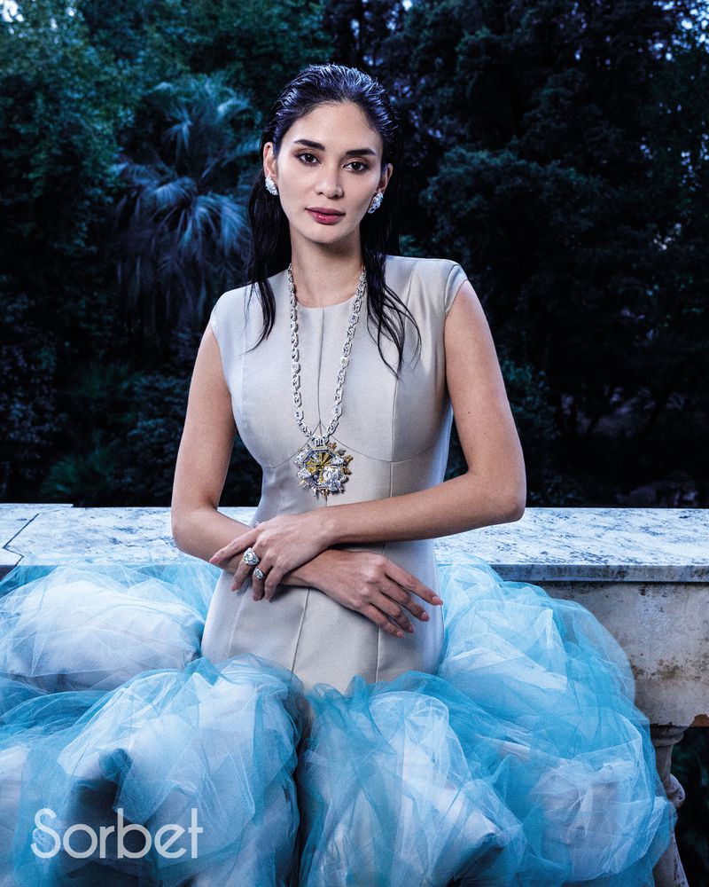 Woman wearing a grey structured top and voluminous blue tulle skirt, posing outdoors with dark hair and fine jewellery for Sorbet Magazine.