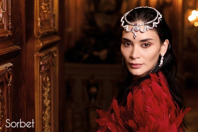 Woman wearing elaborate diamond headpiece and red feather garment in ornate interior for Sorbet Magazine