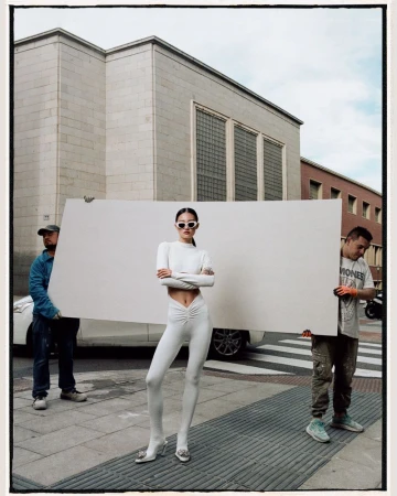Fashion shoot featuring a slender model in an all-white outfit, posing on a city street with men holding a white backdrop.