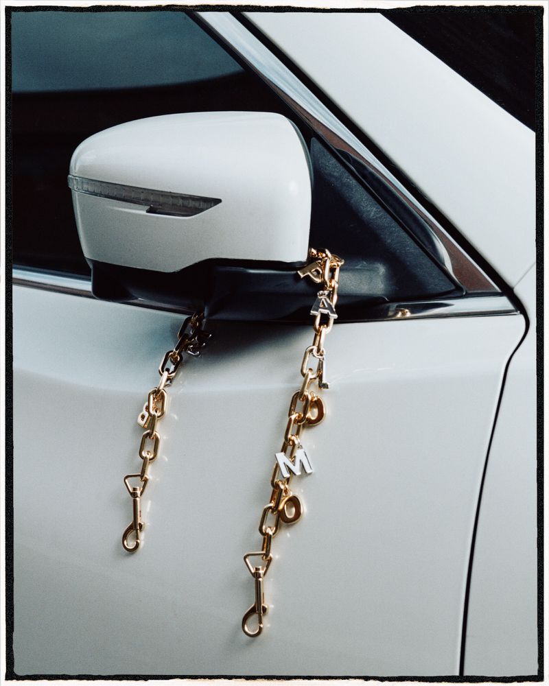 Luxury Automotive Fashion Accessory. Exterior view of a white car side mirror with a gold and silver chain accessory hanging from it.
