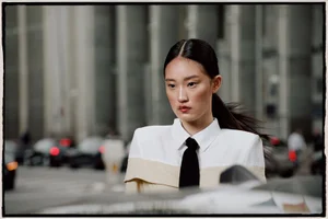Asian woman with dark hair in a white shirt and black tie against a blurred urban street background